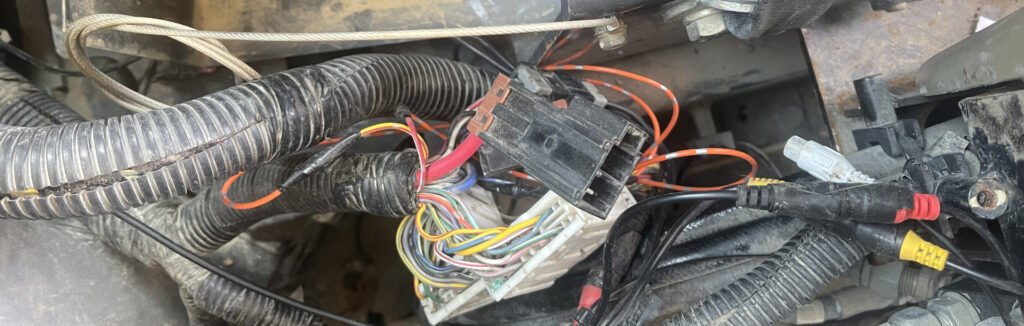 Connector bodies, gathered wires and protective sleeving in a confined electrical area, with a ring-shaped terminal visible near the side.