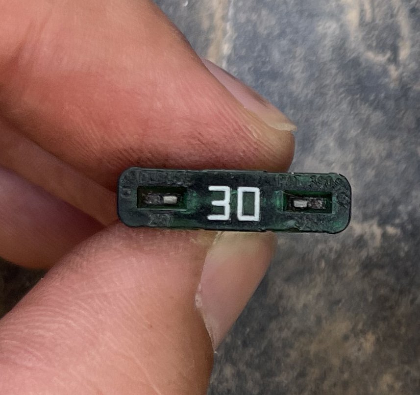 Close-up of a hand holding the green marked face of a small fuse, with the white number 30 visible.