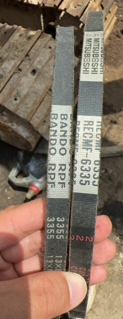 A hand holds two dark textured belt lengths beside one another, showing different light printed panels and visible edge fibers.