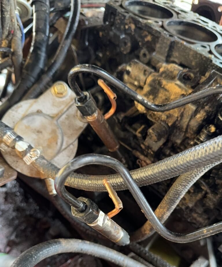 Open engine body with circular openings along its upper edge, rigid curved pipes and braided hoses in the foreground.