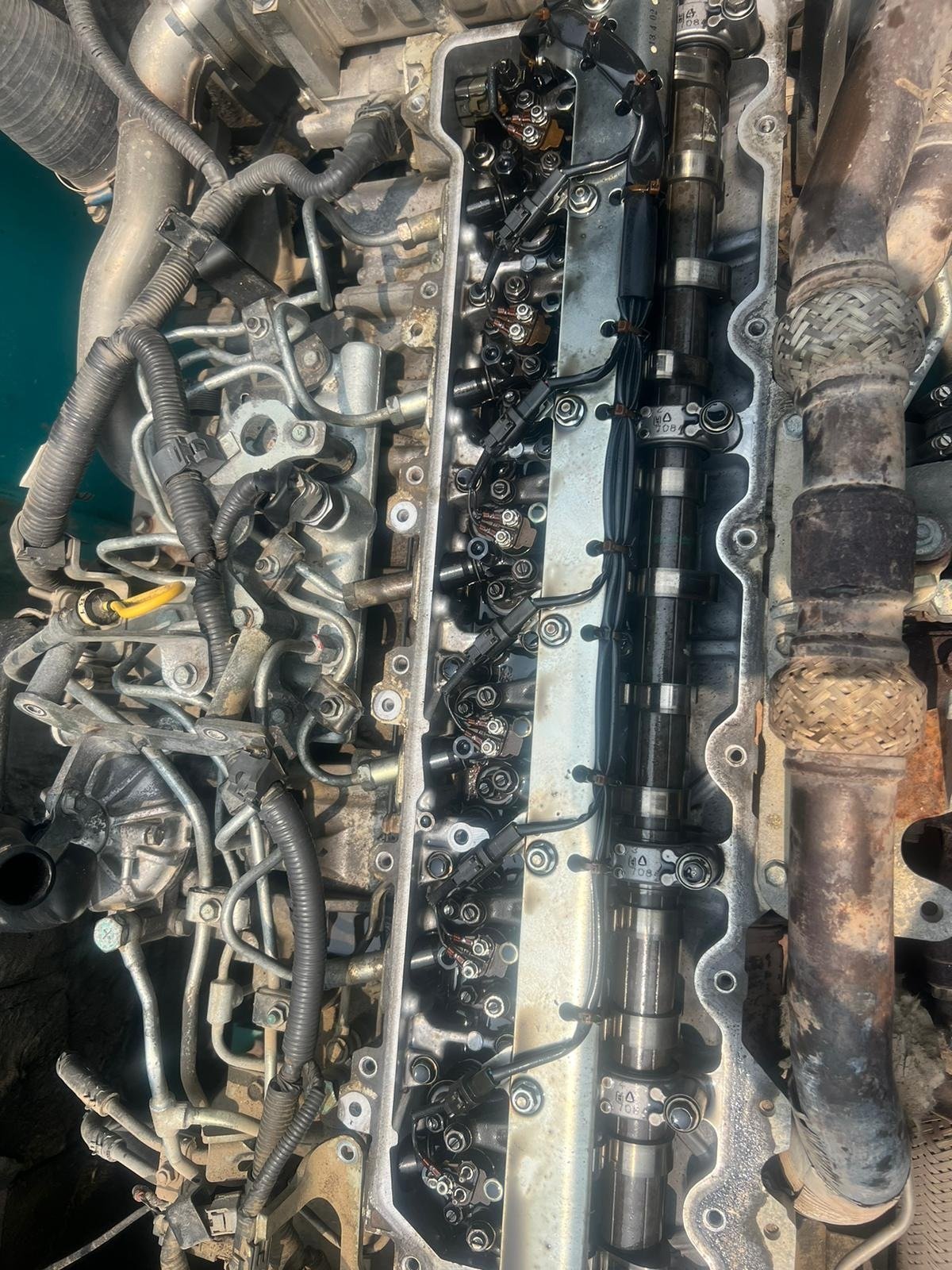 An opened upper engine area with a long shaft, repeated fasteners and surrounding pipes and wiring.