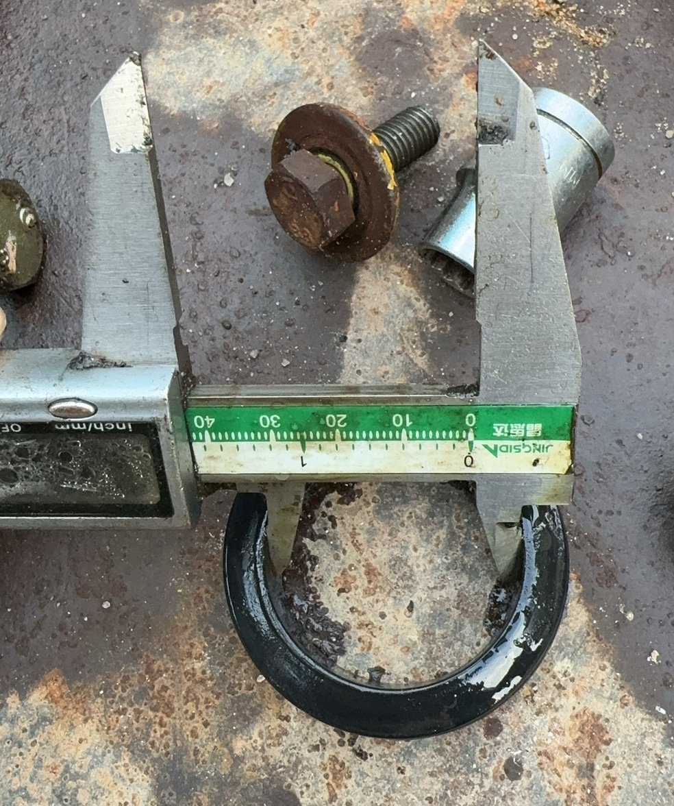 A black open ring-like component and caliper jaws on a work surface.
