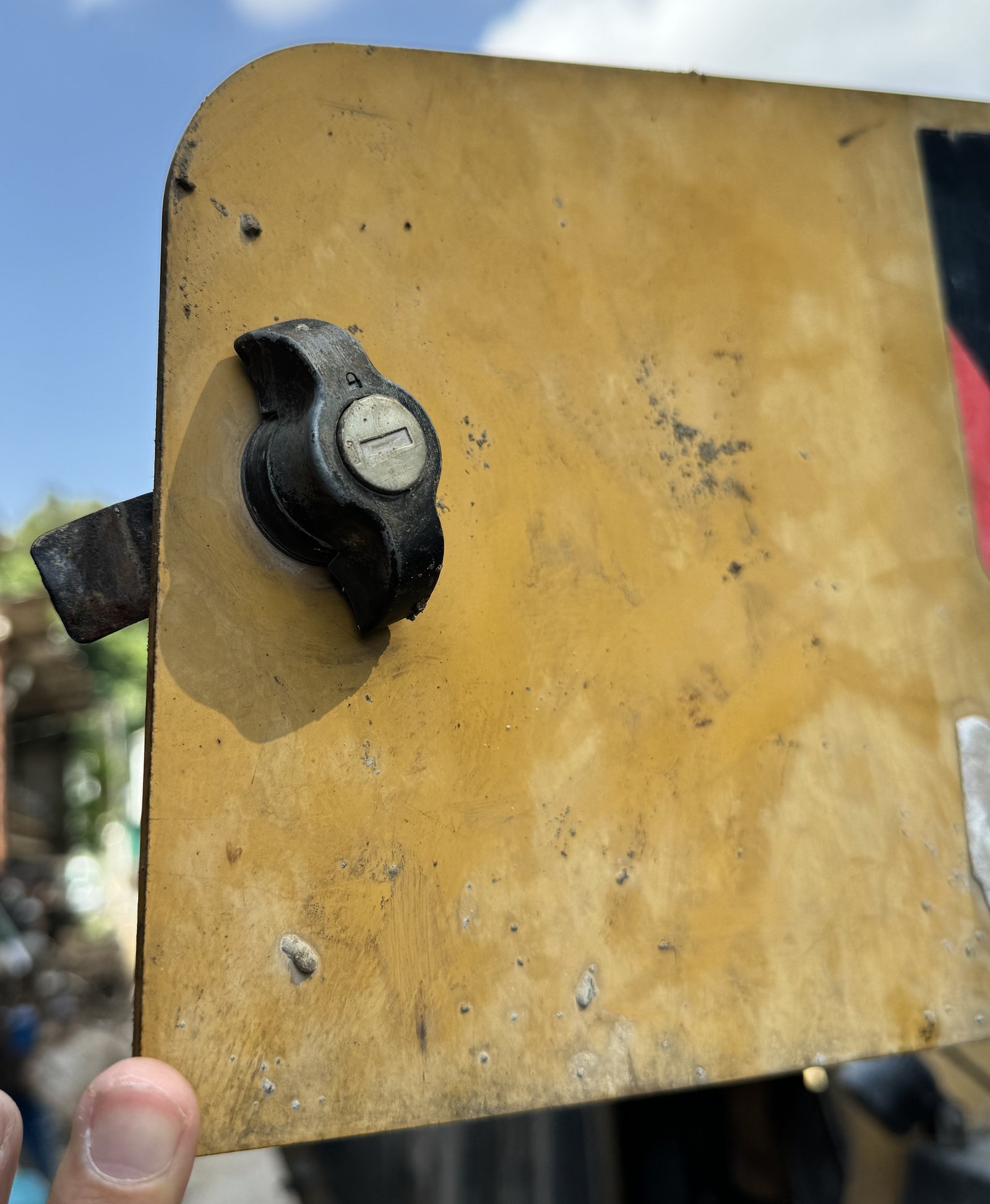 A hand-held yellow access panel with latch and visible surface wear.
