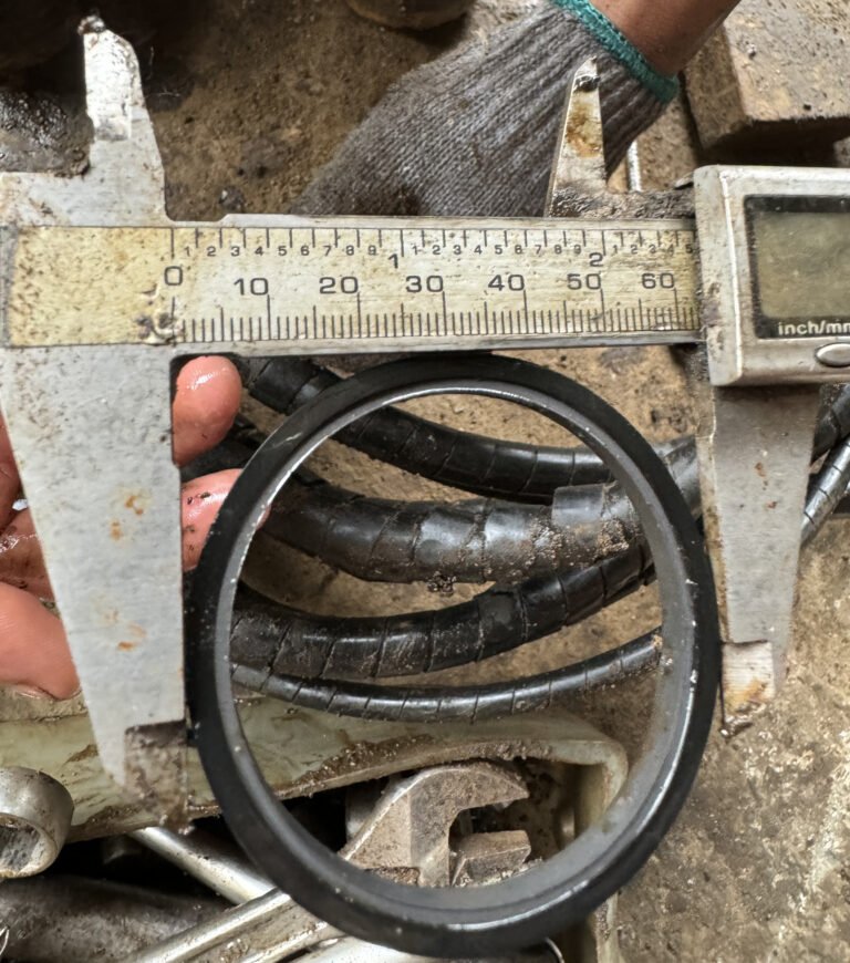 A ring-shaped seal-like item held near caliper jaws with other hoses behind it.