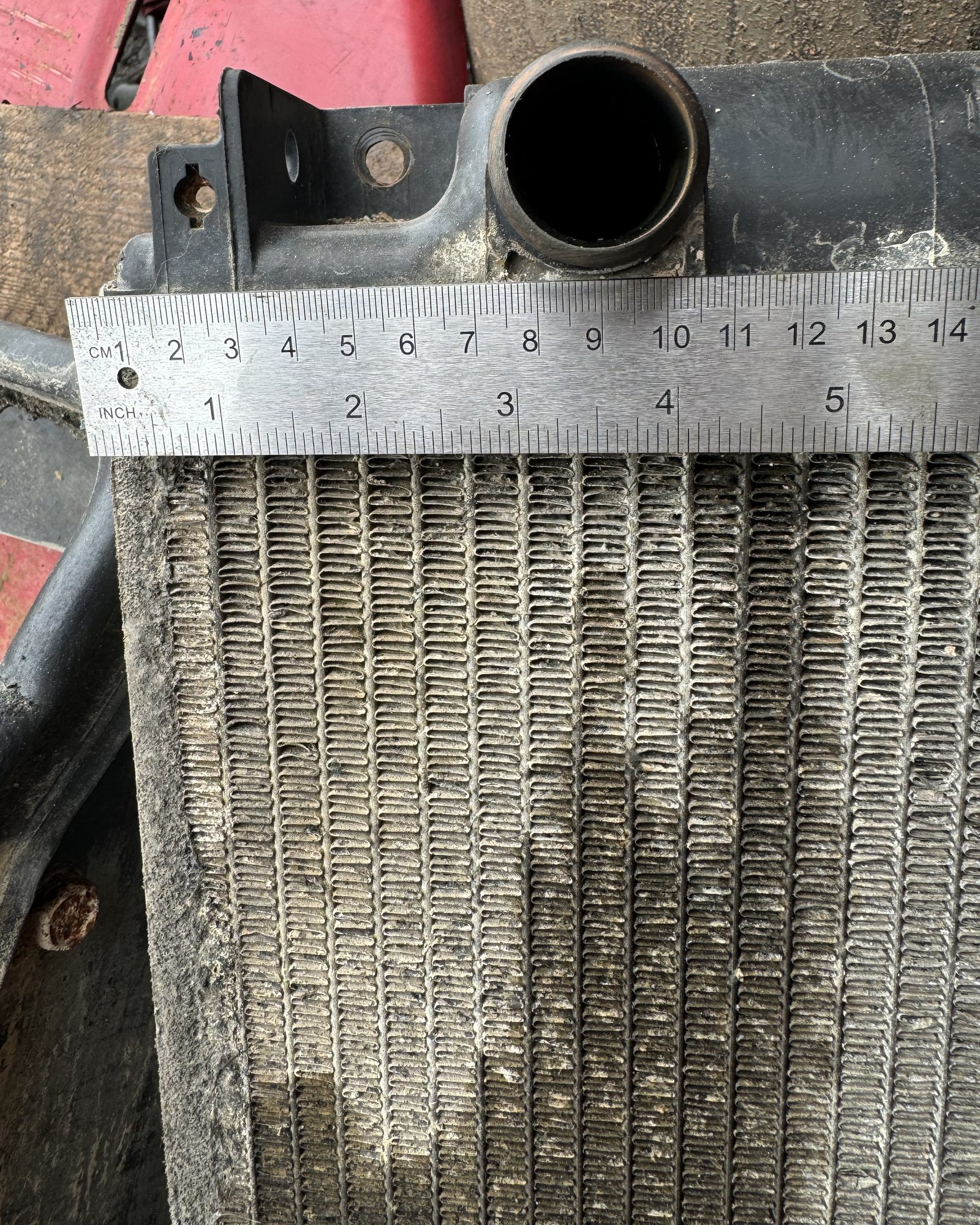 A radiator-like cooling component with a pipe opening, mounting features and a ruler across it.