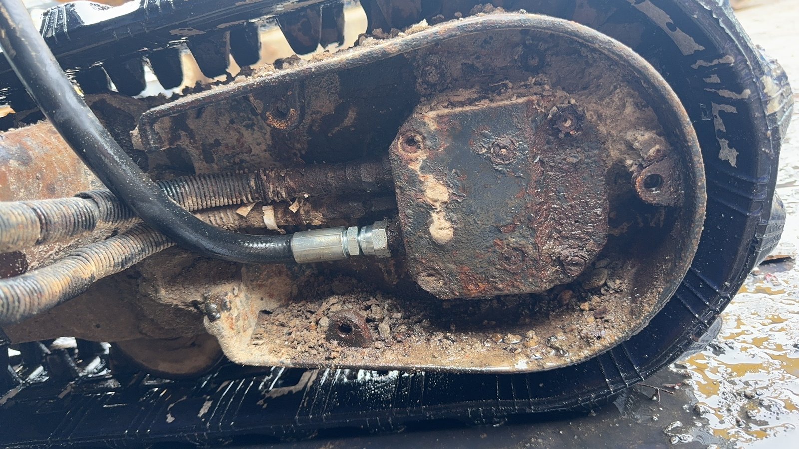 An installed tracked undercarriage housing and connected hose with dirt on surrounding surfaces.