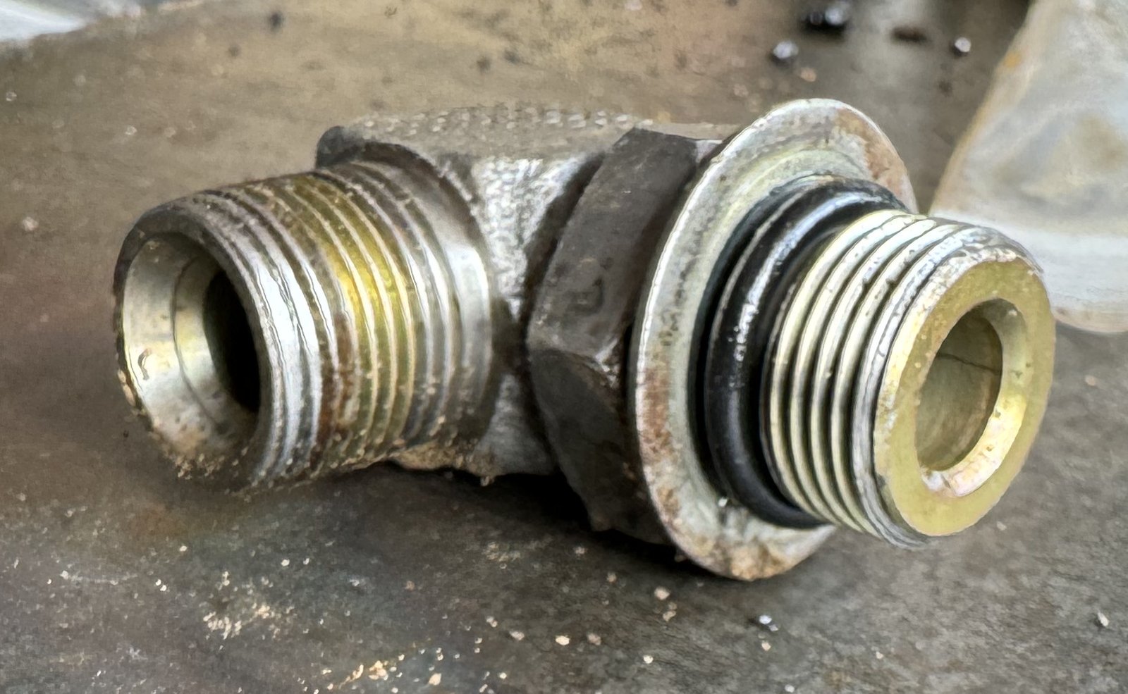 A right-angle metal fitting with two threaded ends and a visible sealing ring.