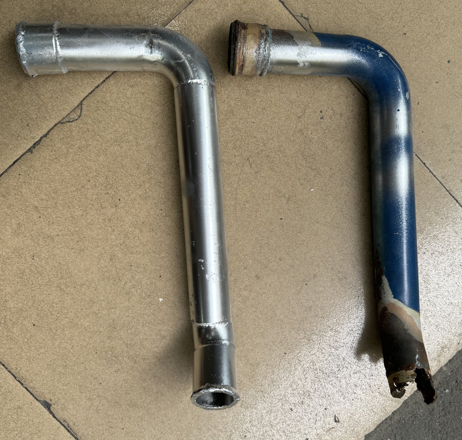 Two bent metal pipes placed side by side, with visibly different end conditions.