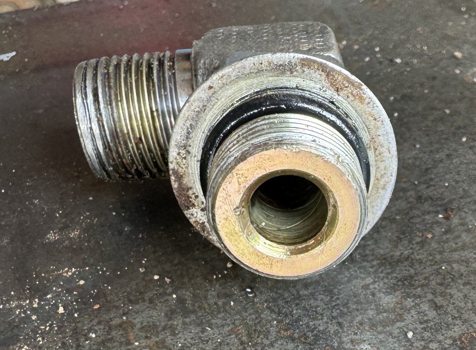Front opening of a metal fitting with external threads, a dark ring-like band and a wider circular feature behind it.