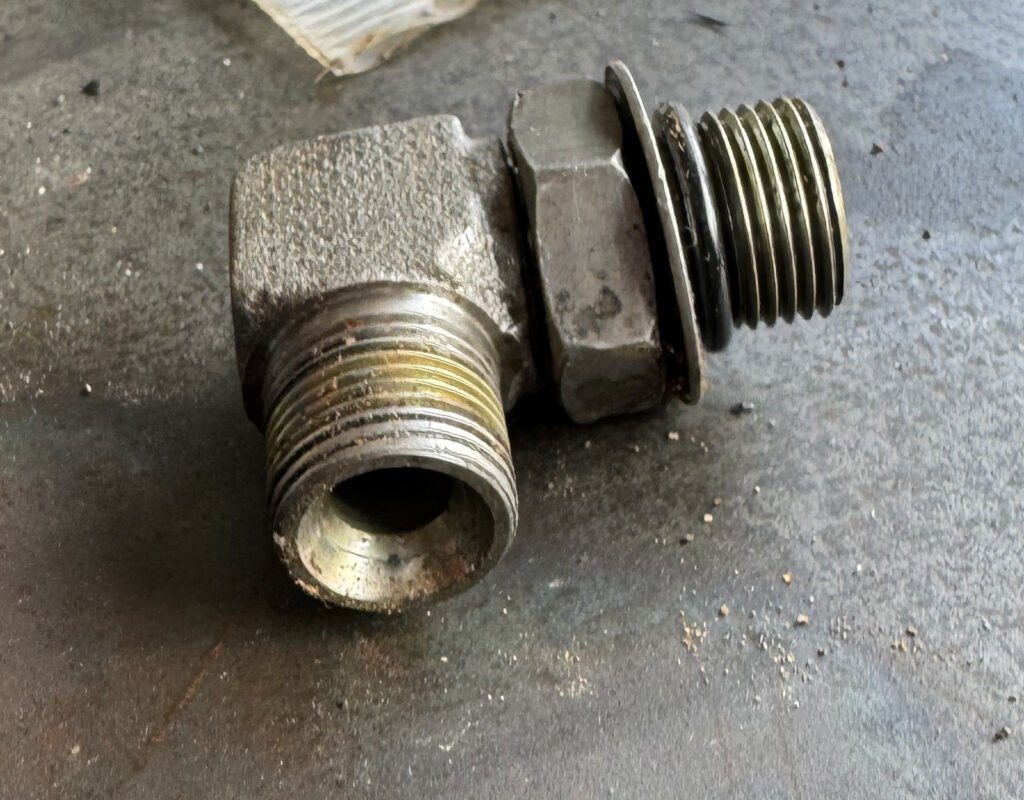 Angled fitting with one circular opening facing the camera and another externally threaded section visible to the side.