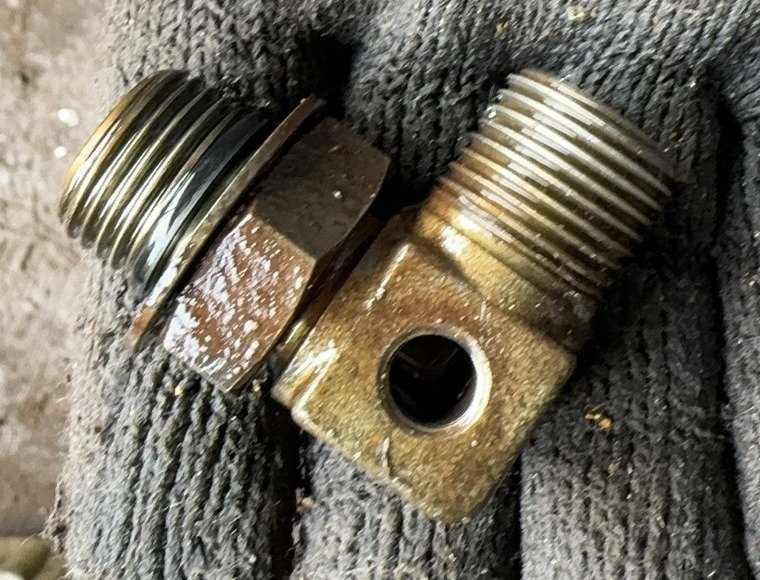 Gold-toned fitting held in a knitted glove, with two externally threaded sections and a circular opening in the body side.