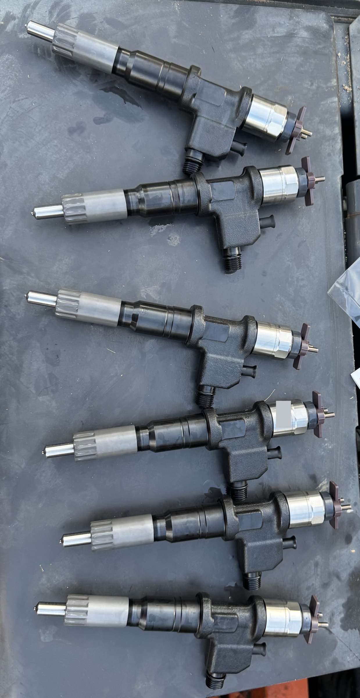 Six long components in separate rows on a grey surface, with silver ends, dark central bodies and shorter projecting features.