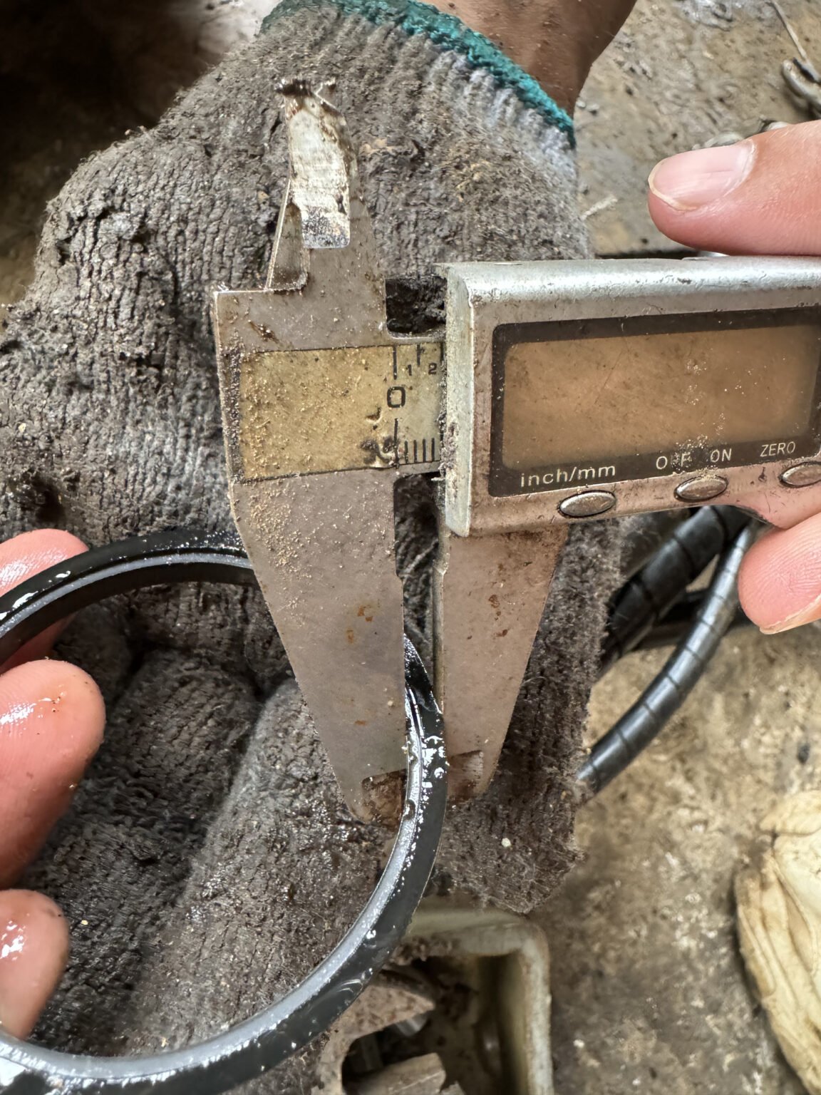 Partial dark ring with a recessed, lip-like edge beside caliper jaws, held against a work glove.