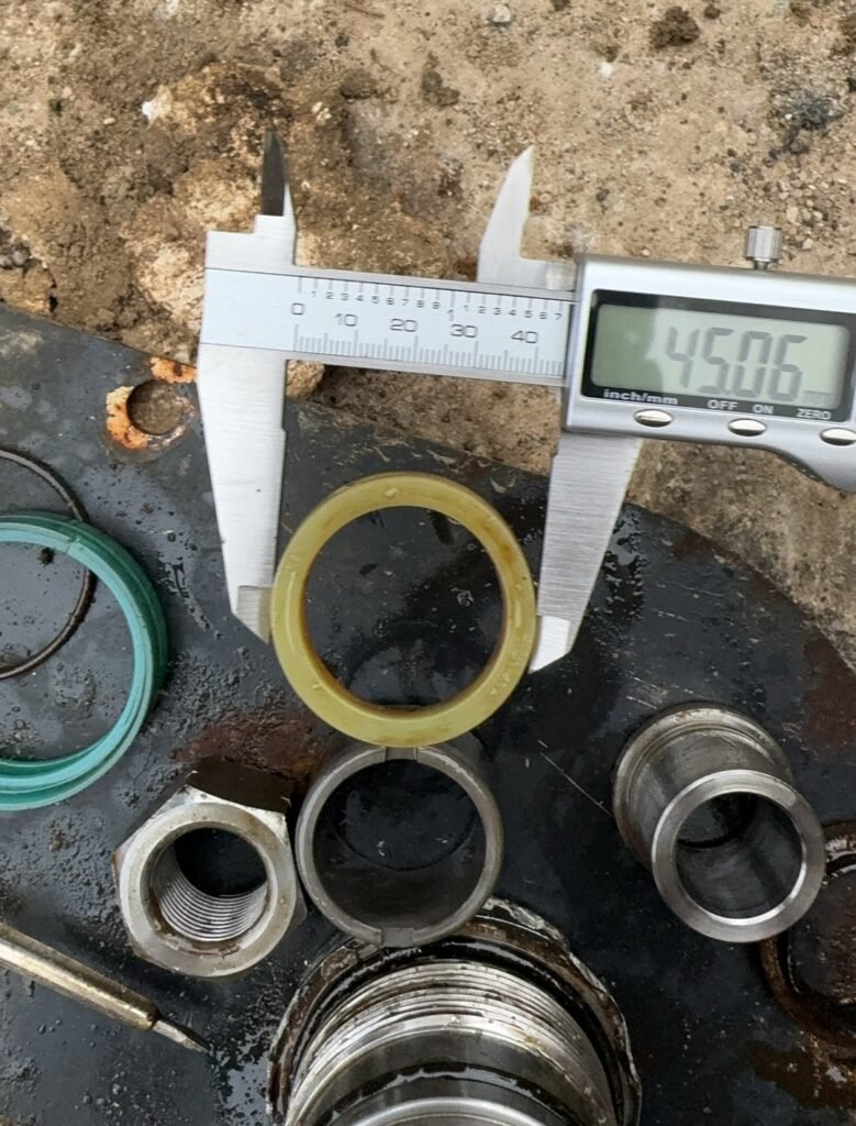 Yellow-toned ring with its opening and outer outline visible between external caliper jaws, with other ring-shaped and metal items nearby.