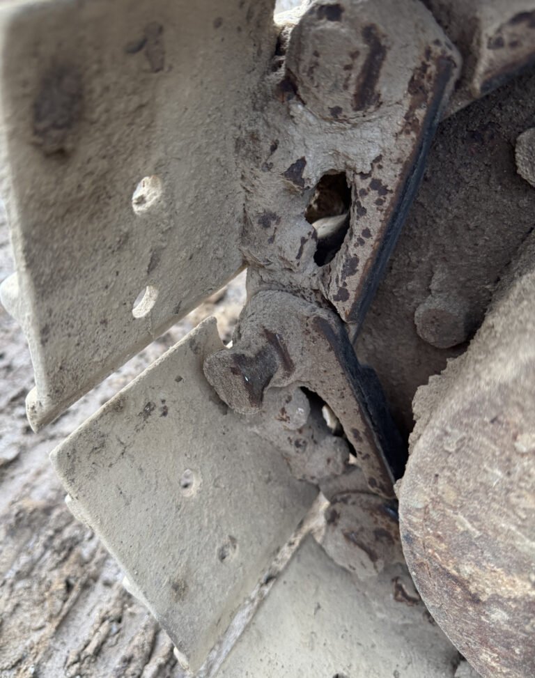 Side detail of projecting track plate edges, a narrower linked section with circular end features and a nearby wheel rim.